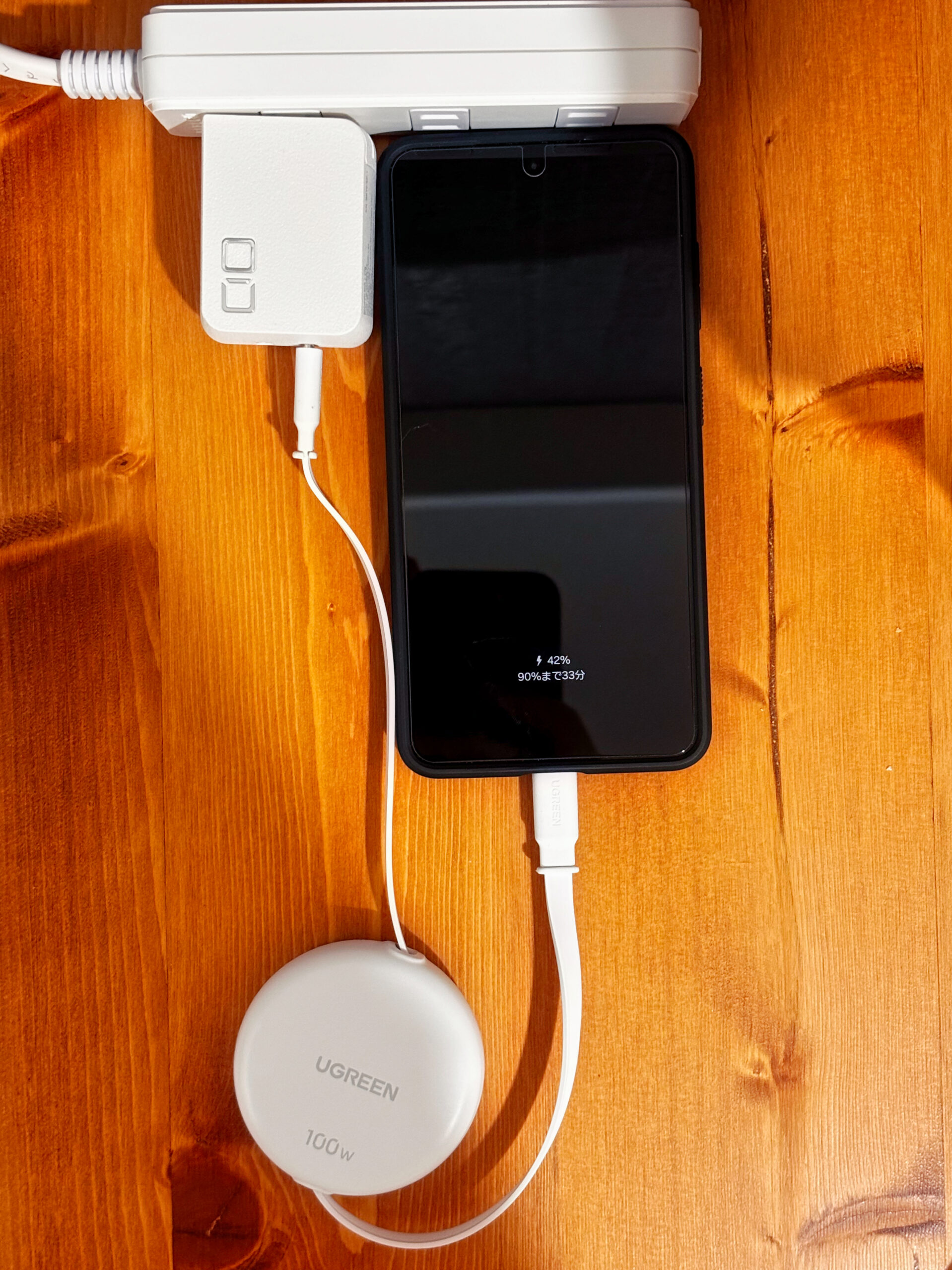 ダイニングの電源タップにCIO充電器が刺さり、UGREENの巻き取りケーブルでスマホを充電している様子